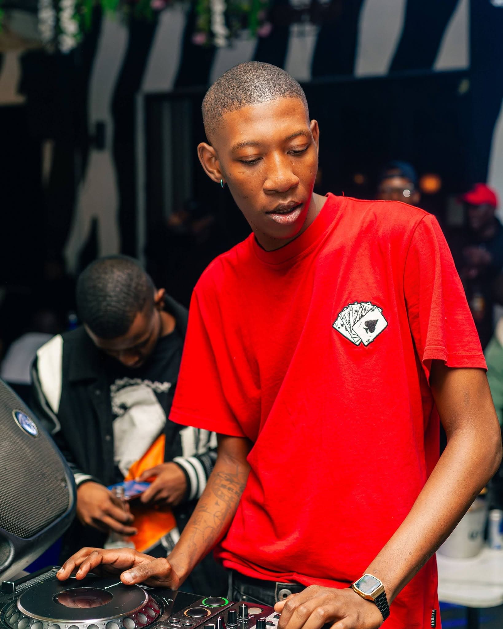 A young DJ works the decks in front of the zebra-print wall, red shirt glowing under the lights.