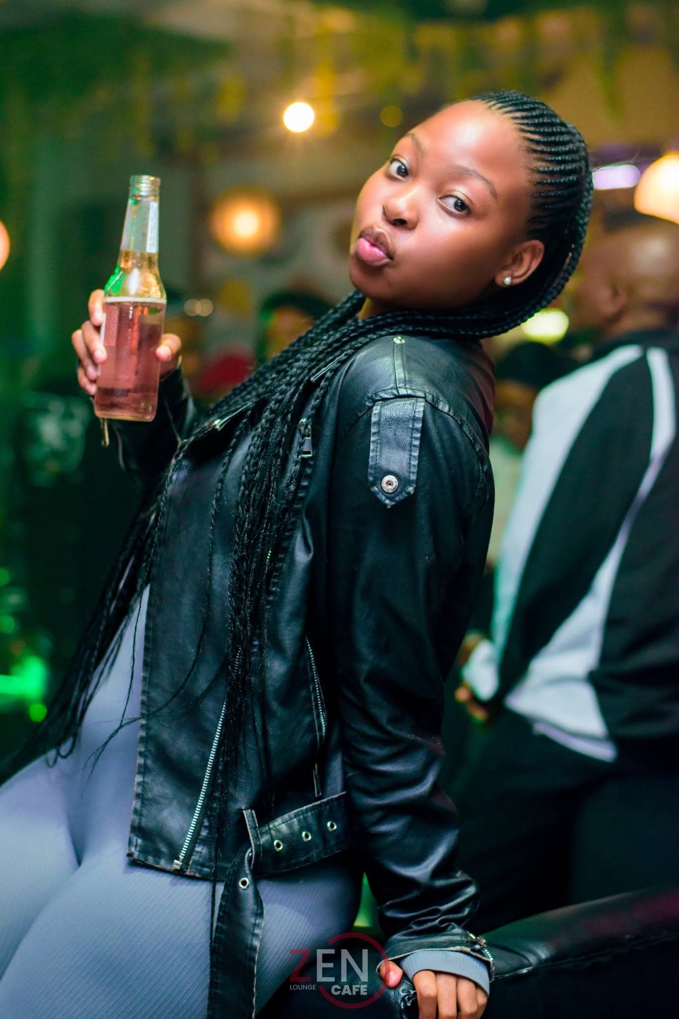 A guest toasts with a bottle under a wash of green lounge light.