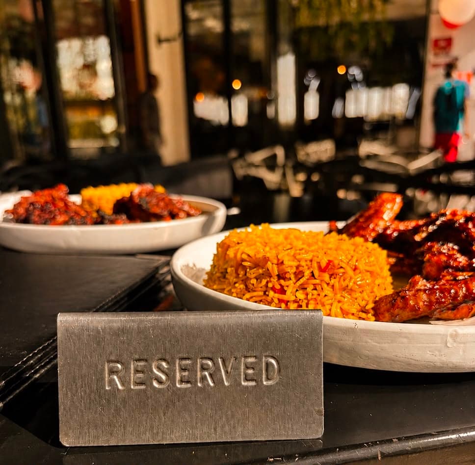 A reserved table set with a bowl of jollof rice and glazed chicken wings, framed by Zen Cafe Lounge's warm, softly blurred dining room.